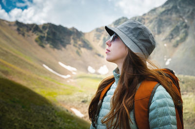Young woman tourist with a backpack and glasses stands in profile, summer portrait, against the