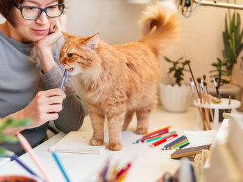 Woman is drawing in notebook. cute ginger cat sits near her. fluffy pet and artist. calming hobby.