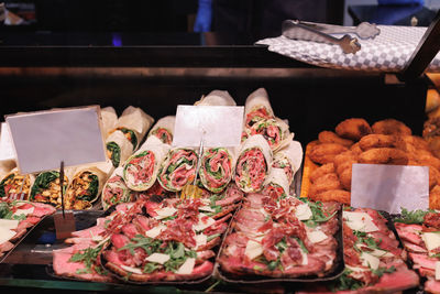 Slices of cut meat on a tray and group of prepared flatbreads filled with meat, cheese and salad.