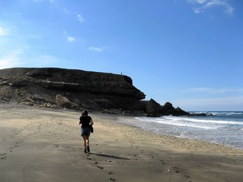 Rear view of man walking on beach against sky