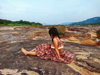 Rear view of woman sitting on mountain against sky