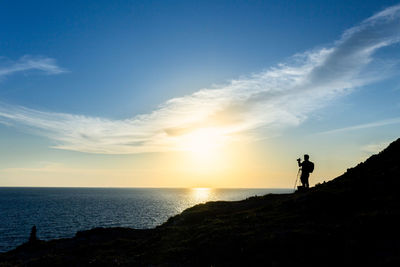 Silhouette person standing on sea against sky during sunset