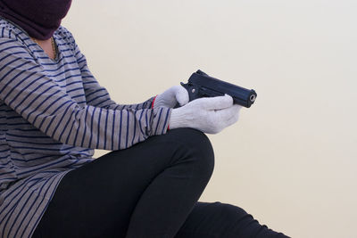 Rear view of man holding gun against wall