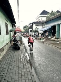 Rear view of man riding bicycle on street against buildings