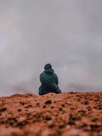 Rear view of man sitting on land against sky