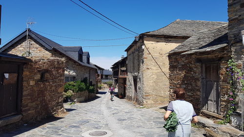 People walking on footpath amidst buildings against sky