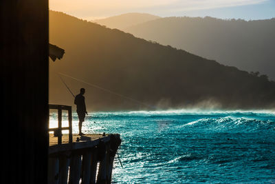 Man fishing in sea against sky during sunset