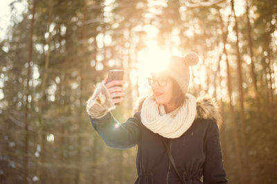 Young woman photographing taking selfie with mobile phone on snow covered field