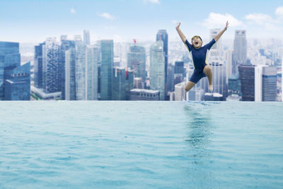 Boy jumping in swimming pool against cityscape