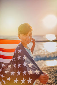 Portrait of boy holding american flag at beach during sunset