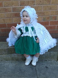 Full length of cute baby girl in dress sitting against brick wall