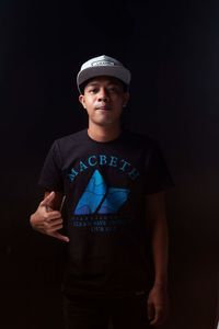 Portrait of young man standing against black background