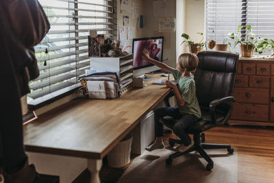 Wide view of young student getting virtual high five from teacher during online class