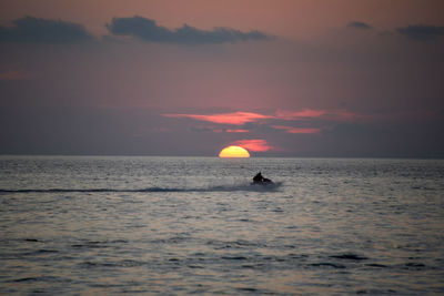 Silhouette people in sea against sky during sunset
