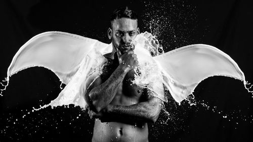 Portrait of shirtless man by milk splashing in angel shape against black background