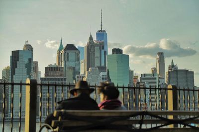 Two men sitting on bench against the cityscape