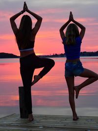 Women exercising on pier over sea against sky during sunset