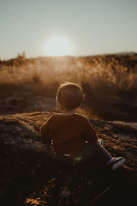 Rear view of boy sitting on field against sky