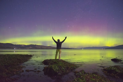 Woman standing in front of lake against sky at night