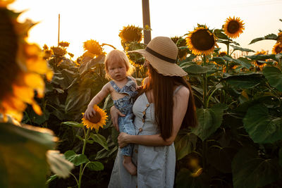 Beautiful mother holds a little son in her arms in a field of sunflowers at sunset