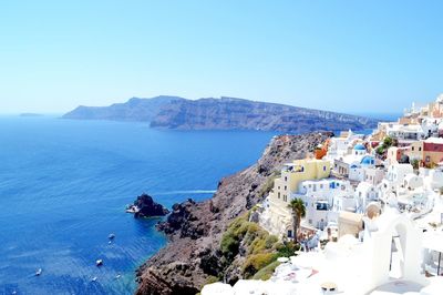 Panoramic view of townscape and mountains by sea against clear sky