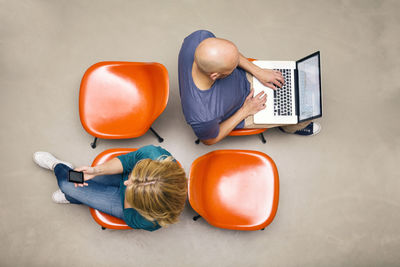 Man and woman sitting on chairs using portable devices