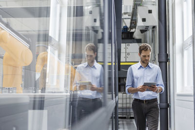 Businessman checking robots with digital tablet in high tech company