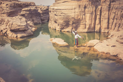 Reflection of woman standing on rock formation in water