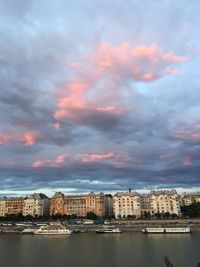 Buildings by river against sky during sunset