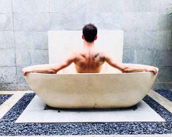 Rear view of shirtless man sitting in bathroom