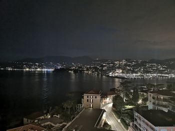 High angle view of illuminated buildings by sea against sky at night