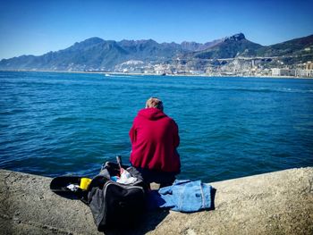 Rear view of person on retaining wall against sea during sunny day