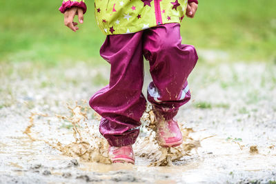 Low section of child playing in puddle on field