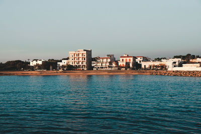 Sea by buildings against clear sky