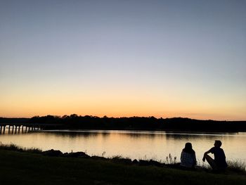 Silhouette people looking at lake against sky during sunset