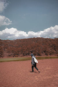 Rear view of man standing on field against sky