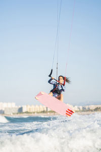 Female kite surfer in swimsuit ridding waves in sea on sunny day in summer