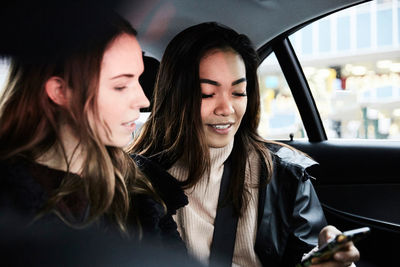 Female friends using mobile phone while riding in taxi at city