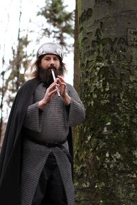 Portrait of man in costume playing flute by tree