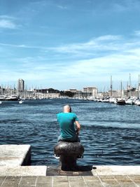 Rear view of man looking at sea against cityscape