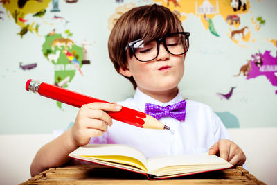 Close-up of cute boy holding large pencil with book at table