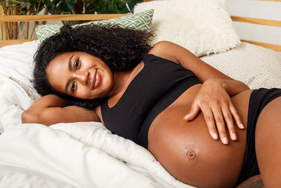 Portrait of smiling pregnant young woman lying on bed