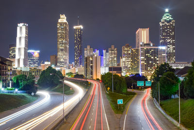 Light trails on road amidst buildings against sky at night