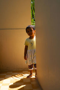 Full length portrait of girl standing by wall outdoors