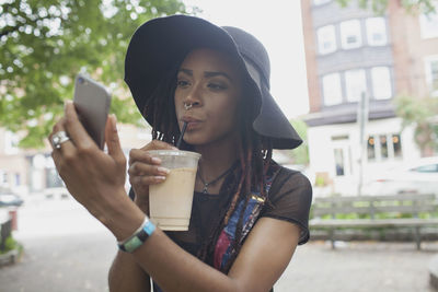 A young woman taking a photograph whilst drinking an iced coffee.