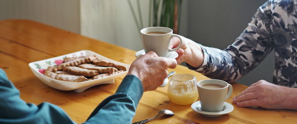 Hands of an elderly couple hold a cup of coffee on the background of the kitchen.