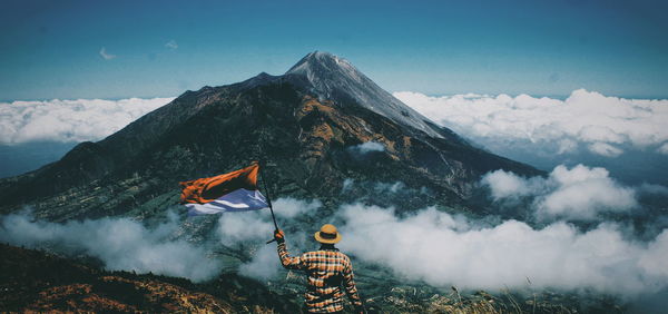 Rear view of man standing on mountain against sky