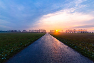 Surface level of road amidst field against sky during sunset