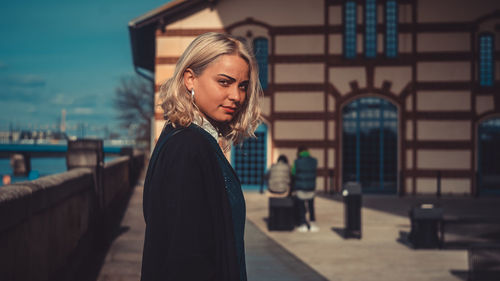 Portrait of young woman standing against building