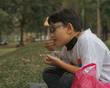 Young hijab asian girl wearing glasses is eating at the park.